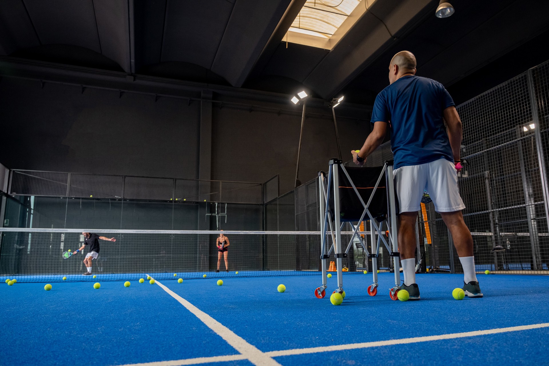 Monitor teaching padel class to man, his student - Trainer teaches boy how to play padel on indoor tennis court