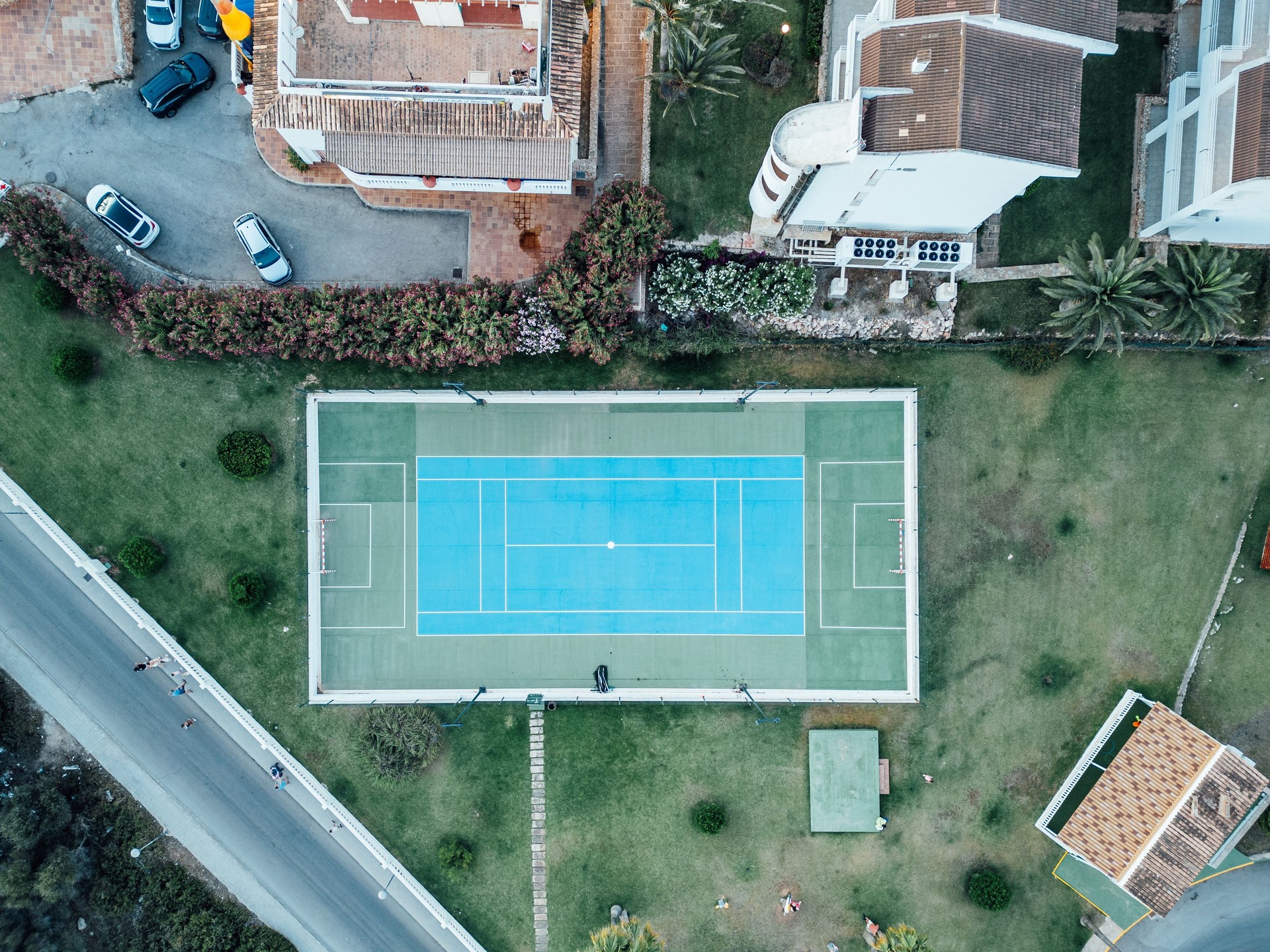 Tennis court from above surrounded by houses and green grass